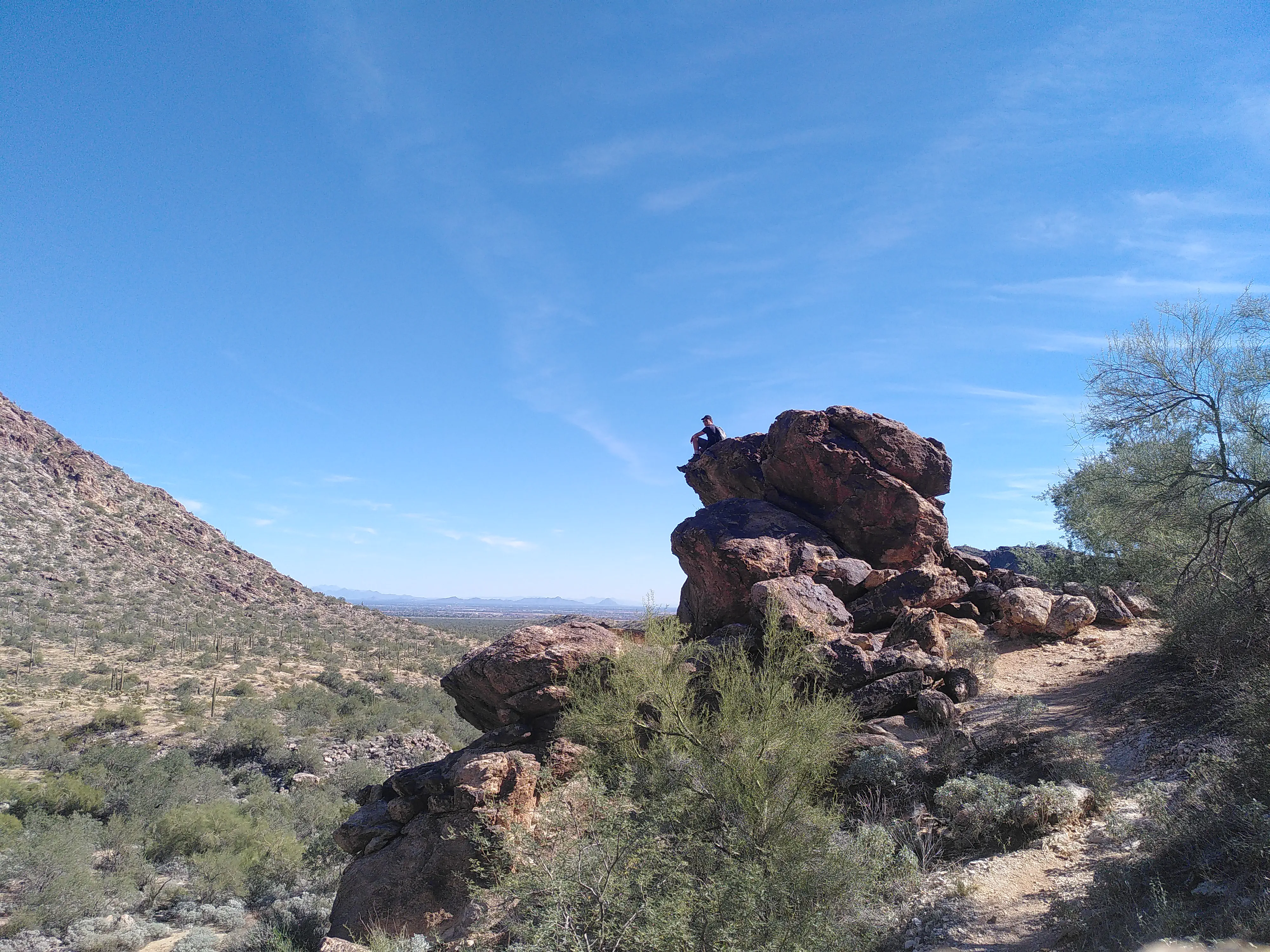 A man sitting on a large rock formation a long distance away