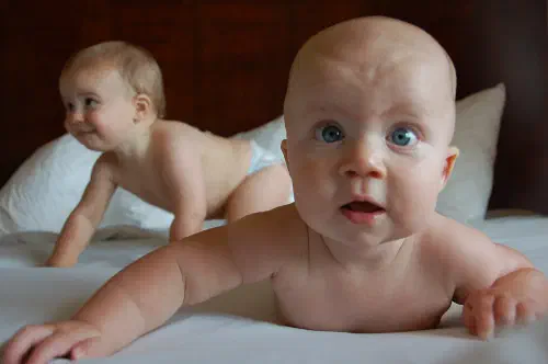 Two babies laying on a bed