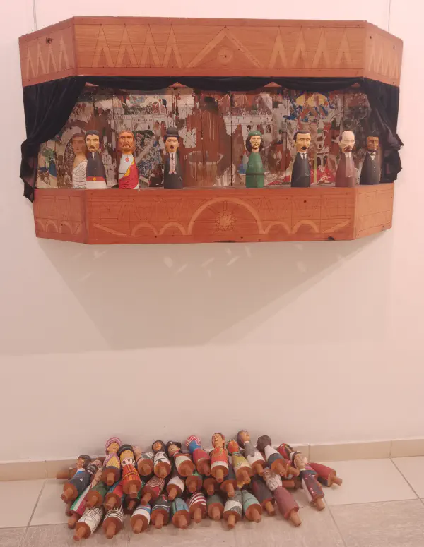 A wall-mounted stage featuring dolls of Che Guevara, Jesus, Charlie Chaplin and more, with a pile of other dolls laying on the floor below it