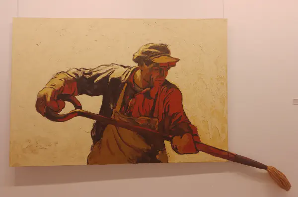 A worker holds the handle of a tool, which extends out of the painting's frame and into a three-dimensional paintbrush