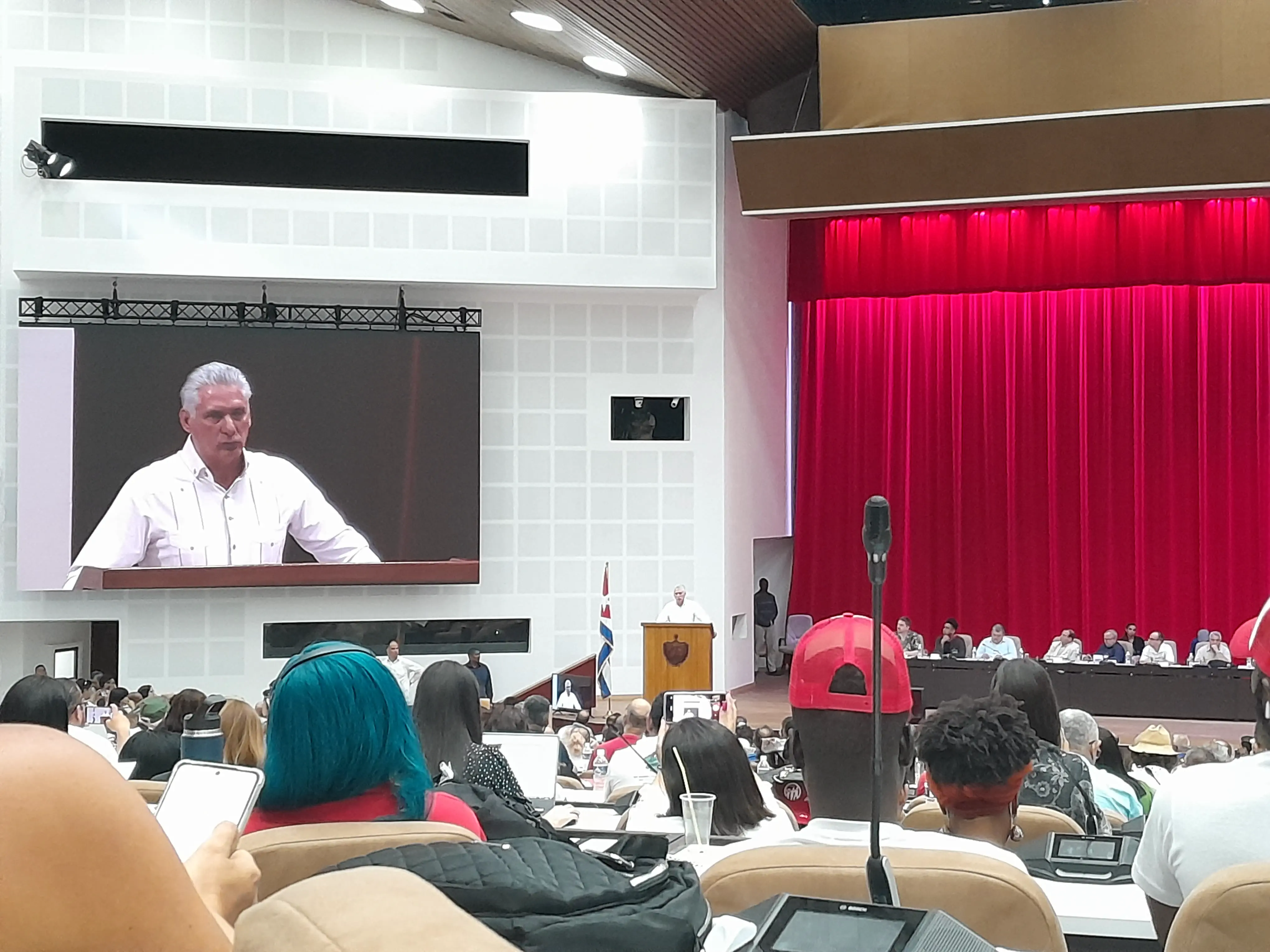 A packed conference hall with a large screen displaying President Miguel Díaz-Canel giving a speech