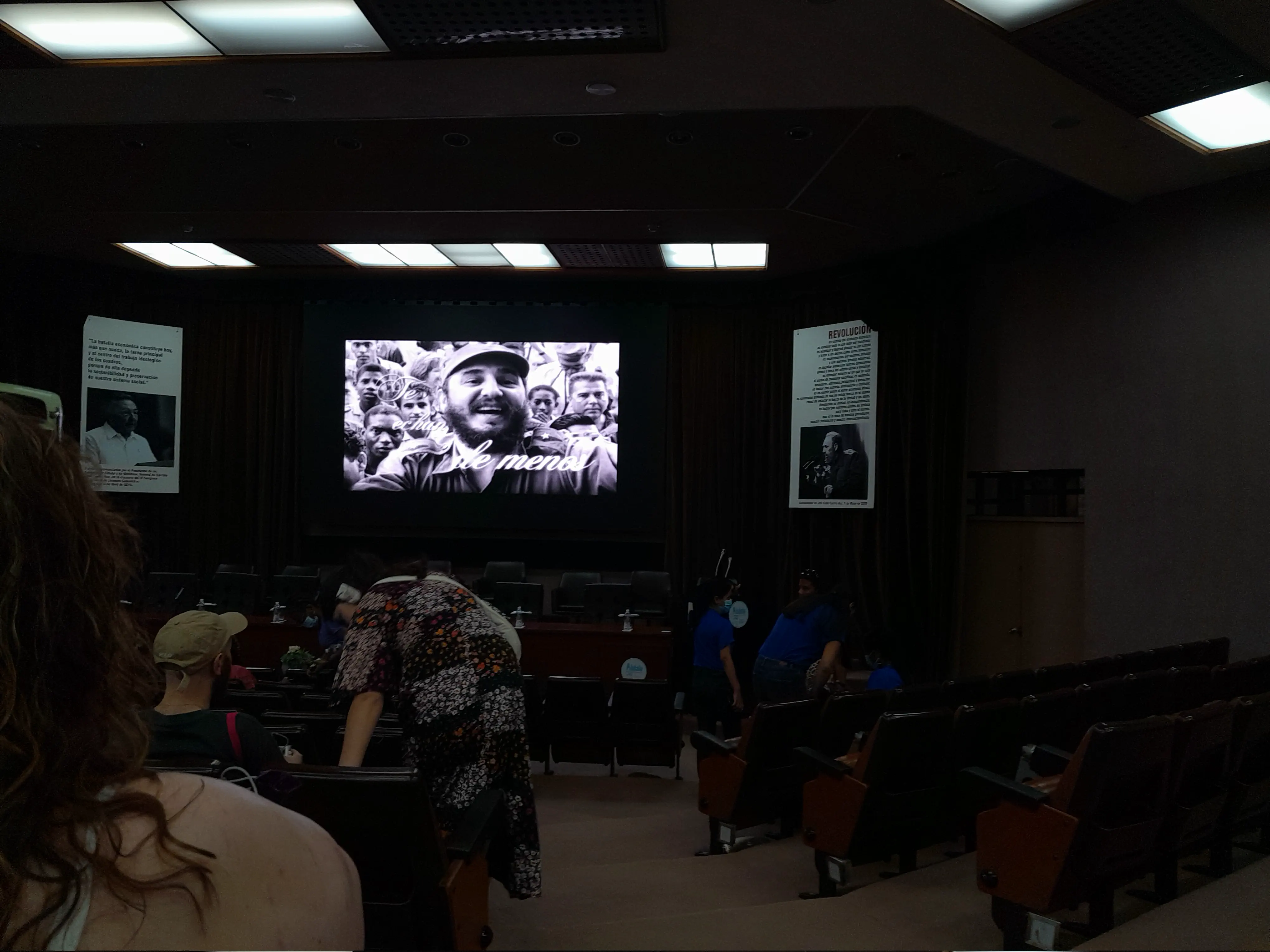 A darkened auditorium with a screen displaying a photo of Fidel Castro and the words ‘te echan de menos’ [you are missed]