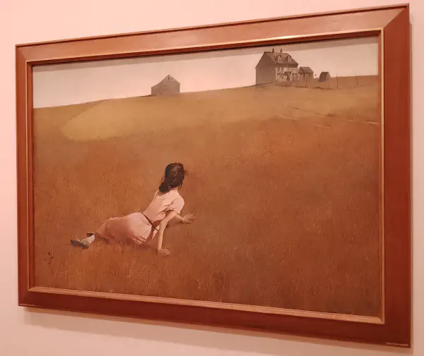 A woman laying in a field looking forwards a distant farmhouse