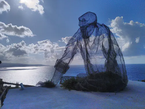 A wireframe statue of a man sat looking out over the Calabrian coastline.