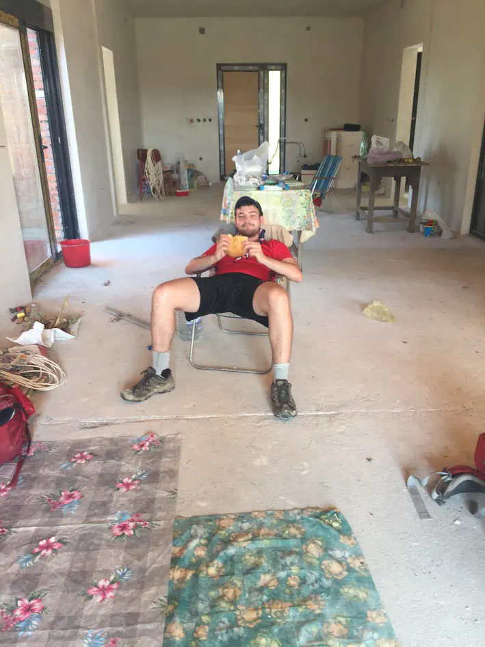 A man reclining inside a construction site, holding a loaf of bread and smiling