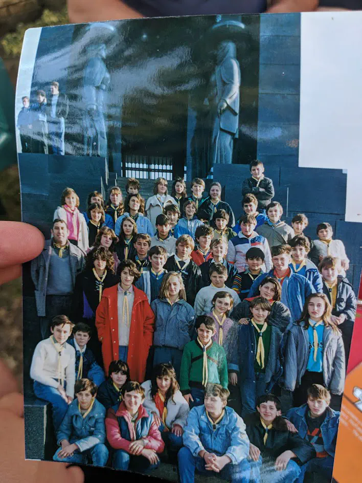 An old photograph depicting a group of Pioneers seated on a set of steps, a monument visible behind them