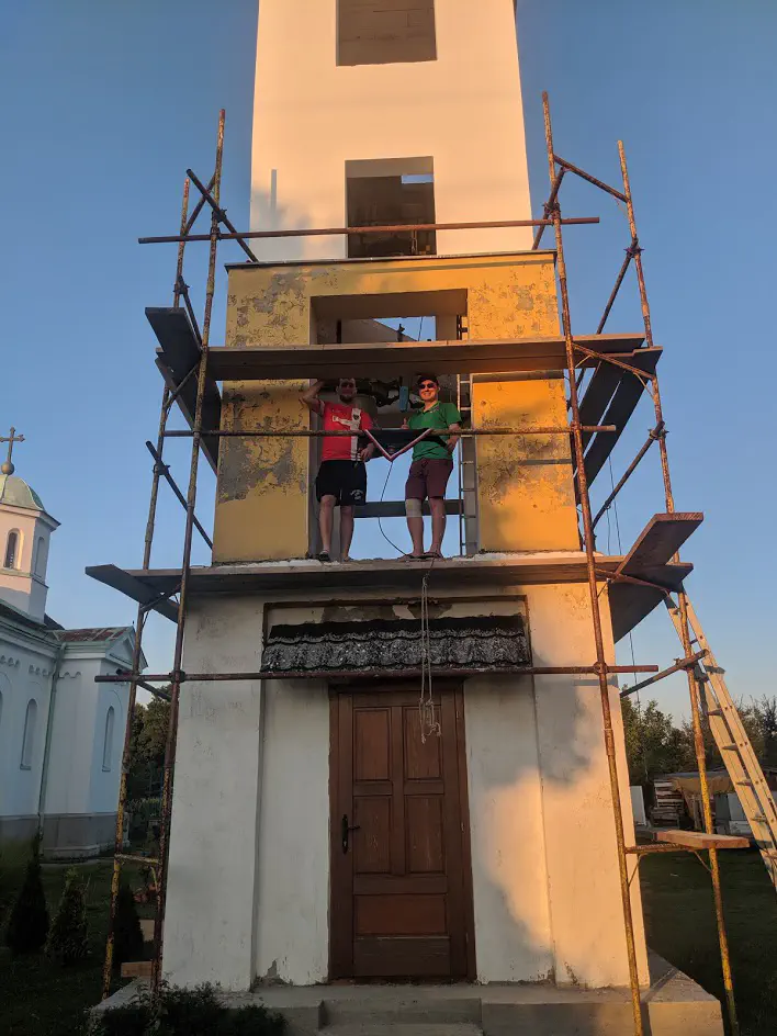Two men standing atop a church tower that is wrapped in scaffolding