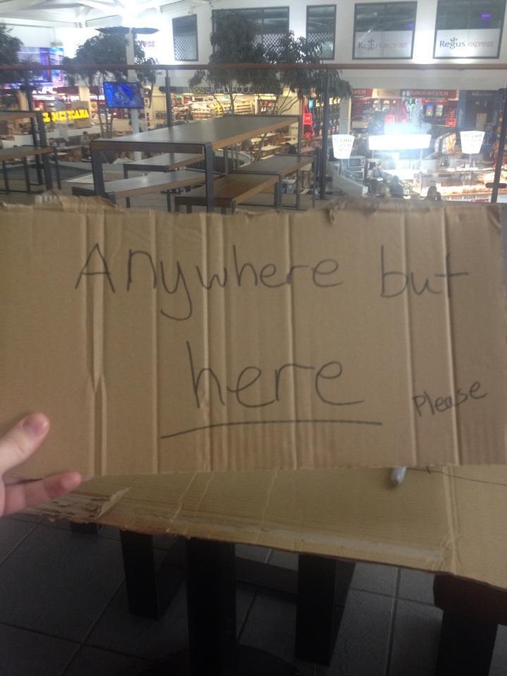 A cardboard sign reading ‘anywhere but here’