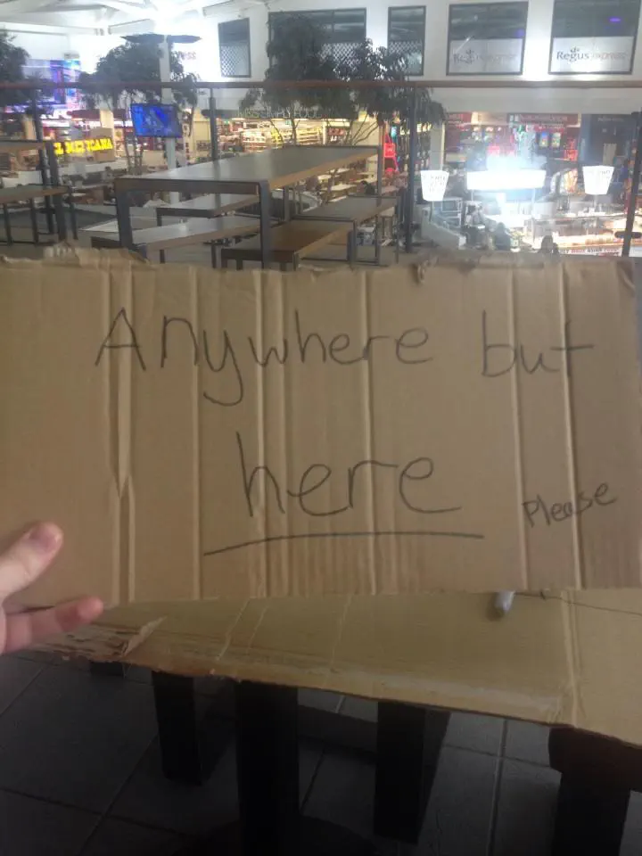 A cardboard sign reading ‘anywhere but here’