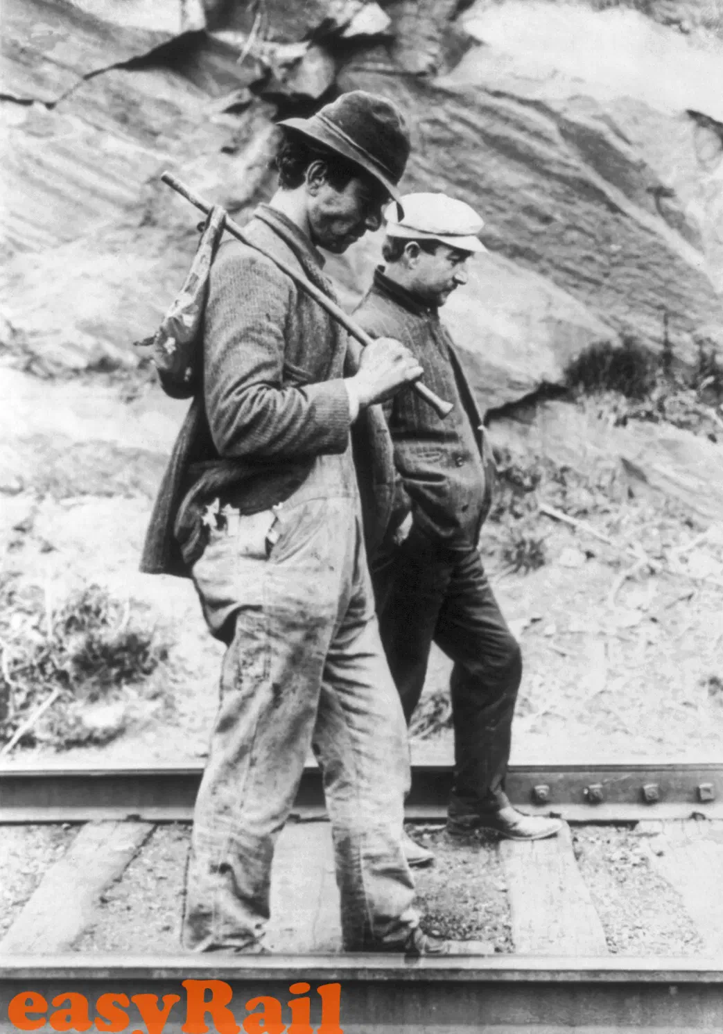 Two hobos walking along a railway track, one carrying a bindle