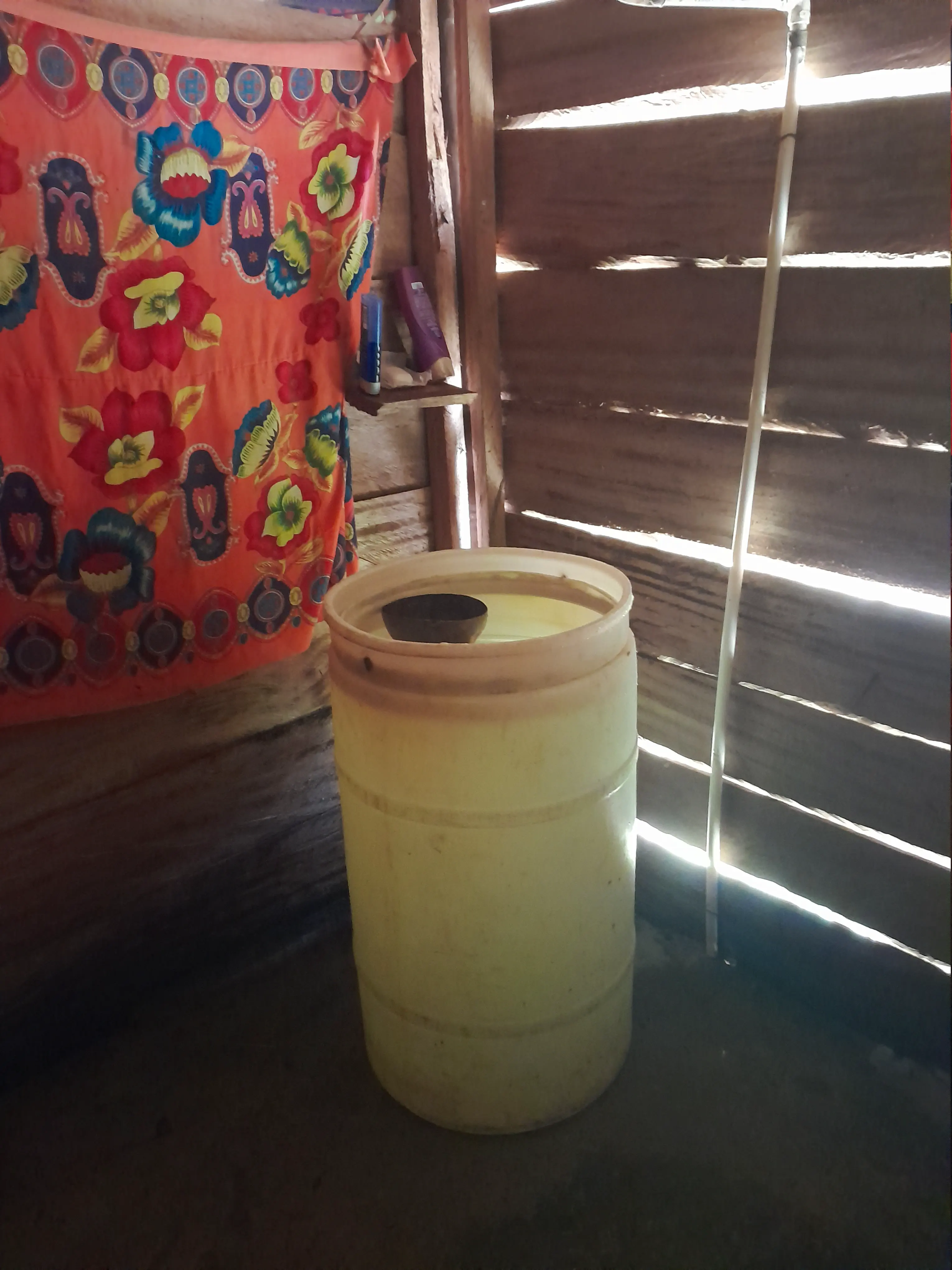 A large water barrel with a halved coconut shell floating in it