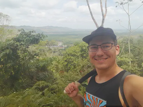 The author in the foreground, resting a machete on his shoulder, with a small village surrounded by jungle in the background