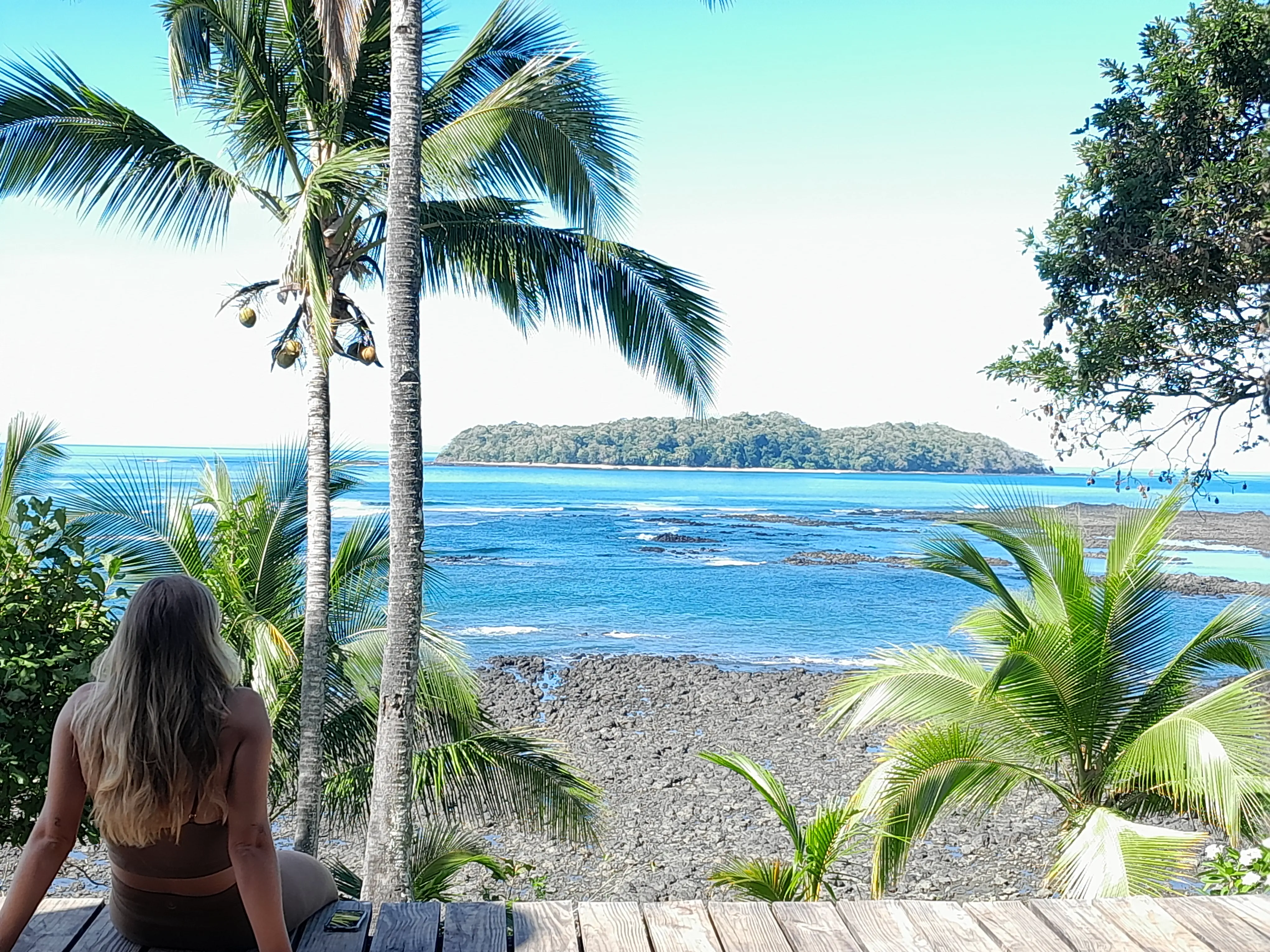 Looking out over the sea towards a distant island, a women sitting on a wooden deck in the foreground