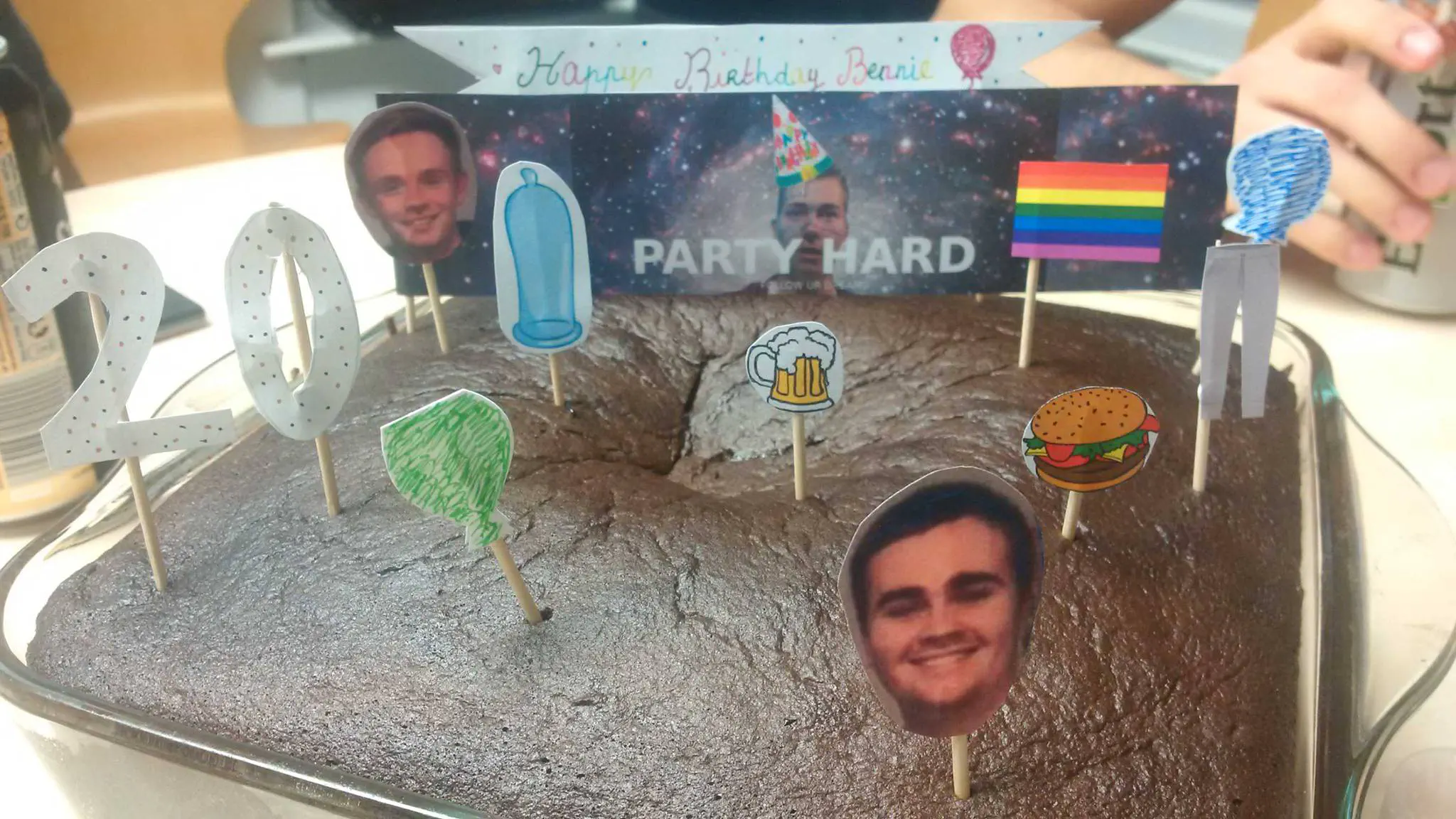 A birthday cake topped with a banner featuring my face and the words 'Party Hard'