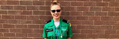 A woman in a St John Ambulance uniform smiling in front of a brick wall