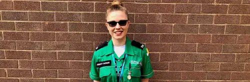 A woman in a St John Ambulance uniform smiling in front of a brick wall