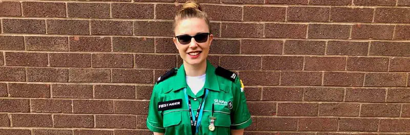 A woman in a St John Ambulance uniform smiling in front of a brick wall