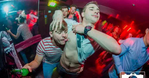 One man licking another man's nipple in a nightclub