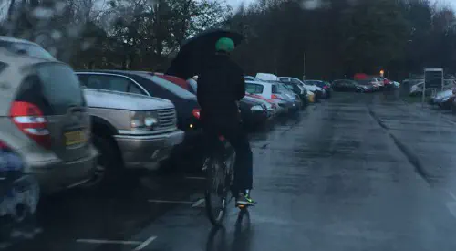 A cyclist riding whilst holding an umbrella