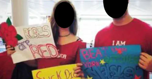 Two people holding cardboard signs reading 'Roses are red' and 'suck a dick York'