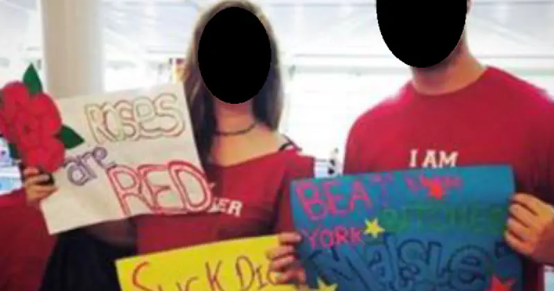 Two people holding cardboard signs reading 'Roses are red' and 'suck a dick York'